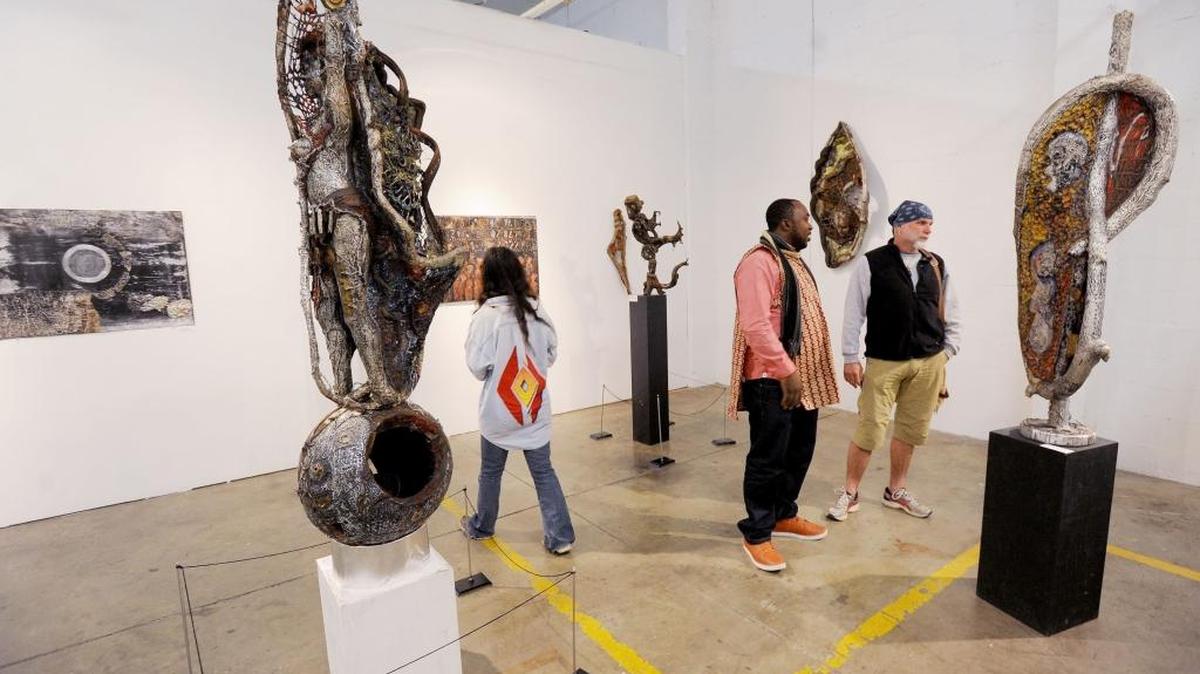 Artist Jean Michel Dissake of Yaounde, Cameroon (center) talks with sculptor Jim Adams (right) in the Cameron Gallery at The Scrap Exchange.