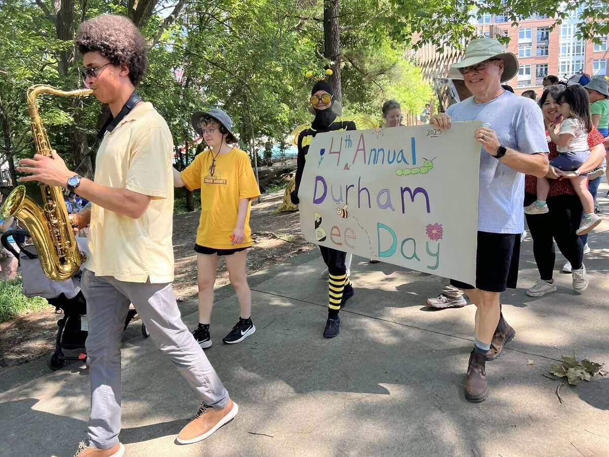 A saxophonist leads a group of people, some dressed as bees, in a parade.