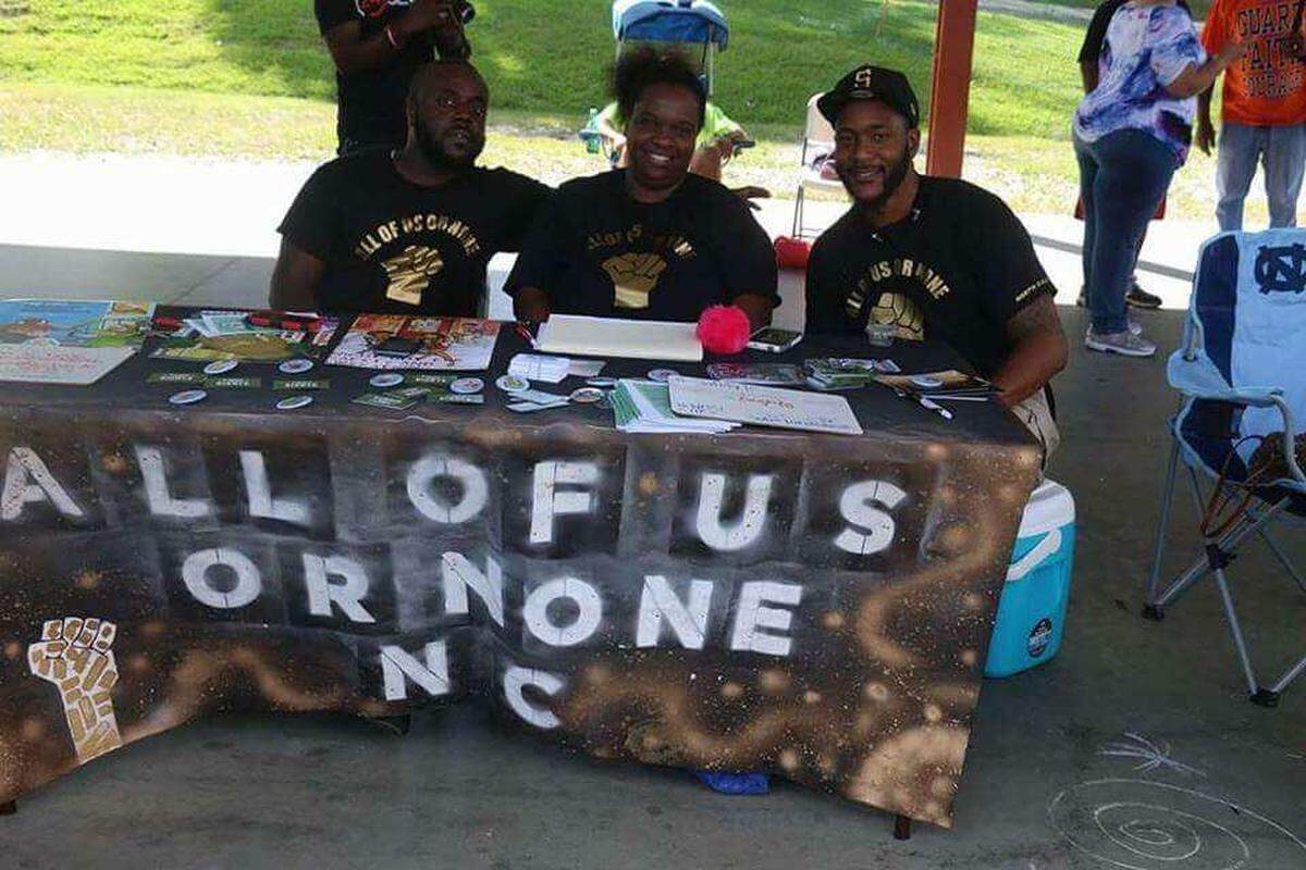 (Left to Right) Brian Rashad Wiley sits with Andraé Muffin Hudson and Umar Muhammad at the "All of Us or None" table at Durham's Black August in The Park festival.