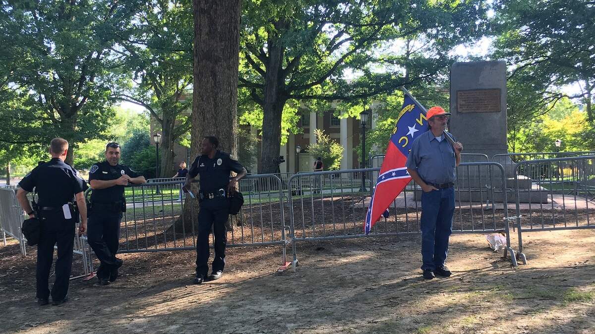 A lone protester stands near police officers near the base of where the Silent Sam statue stood on the campus of UNC Saturday morning, Aug. 25, 2018.