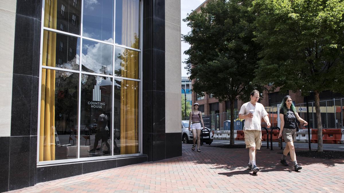Pedestrians walk past 21c Museum Hotel's bar, Counting House, to the cross walk at Main Street and Corcoran Street on Thursday July 5, 2018. A camera, which will count pedestrians as they walk past, sits in the window of the bar.