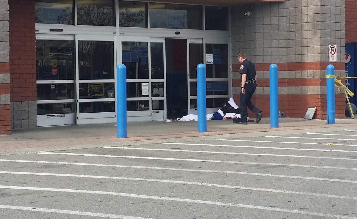 A law enforcement officer approaches a man who has been shot in the side and lying at the entrance to the Walmart store in New Hope Commons in Durham, NC, shortly after 3 p.m. Wednesday, March 28, 2018.