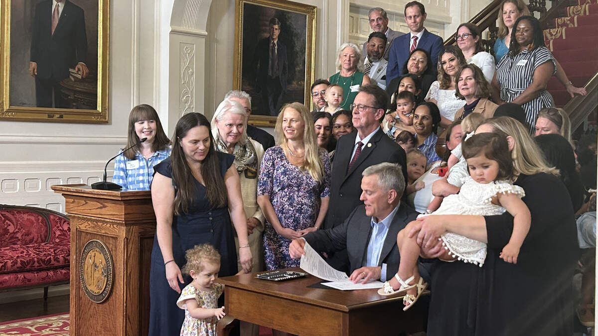 Gov. Josh Stein, surrounded by parents and their young children, signs a bill that extends paid parental leave for state employees to 12 weeks and overhauls state human resources.