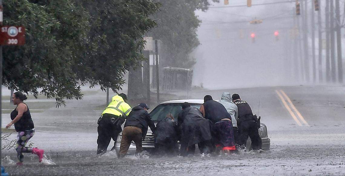 As torrential rain fell Saturday afternoon in Lumberton, NC, police officers helped civilians push a stranded motorist out of the flood water near downtown. 