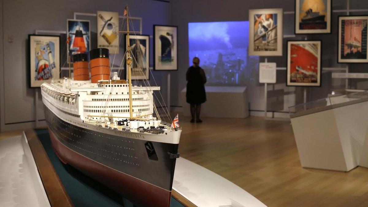 In this May 18, 2017 photo, a visitor views newsreel footage near a model of the Queen Elizabeth at an exhibition entitled “Ocean Liners: Glamour, Speed, and Style” at the Peabody Essex Museum, in Salem, Mass. The new exhibition of more than 200 artworks from around the globe pays homage to the ocean liner era.