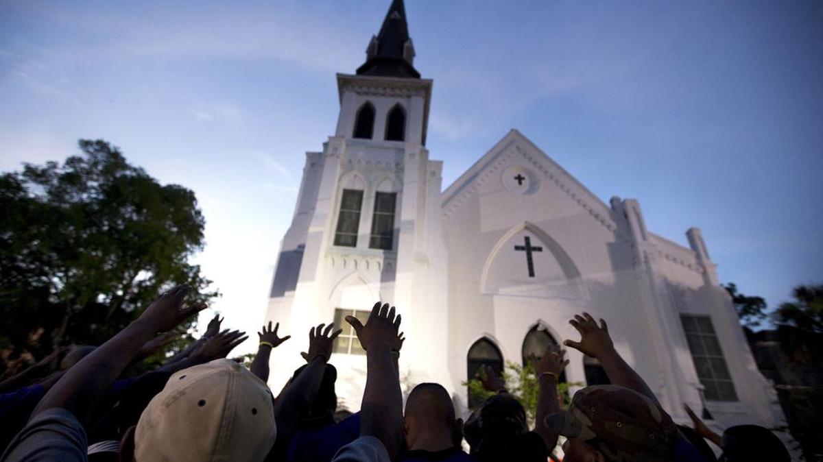 In this June 19, 2015 file photo, the men of Omega Psi Phi Fraternity Inc. lead a crowd of people in prayer outside the Emanuel AME Church after a memorial for the nine people killed by Dylann Roof in Charleston, S.C. The pastor of the church on Saturday announced the designer of a memorial to the nine people killed in the church’s fellowship hall in a racist massacre two years ago.
