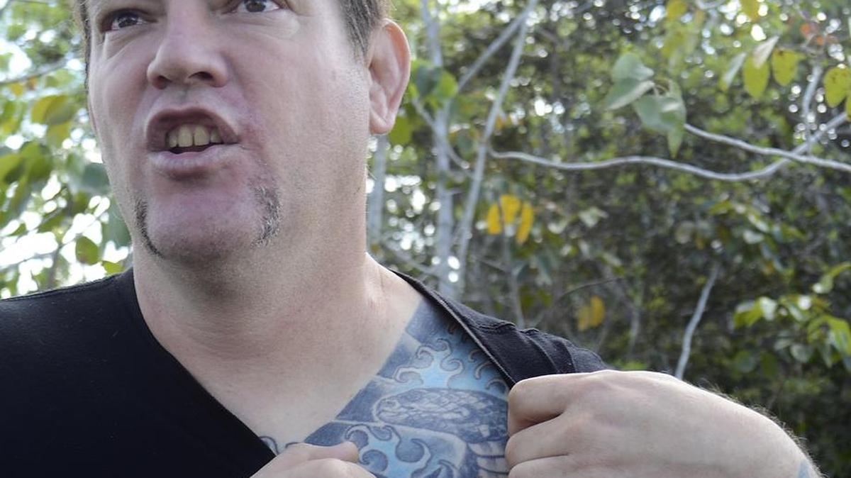 In this March 30, 2017, photo, Brian Hargrove, of Cutler Bay, Fla., pulls down his T-shirt to show a cobra tattooed on his chest while hunting invasive Burmese pythons in the Florida Everglades. Hargrove was hired by the district to kill pythons on the district’s property near the Florida Everglades. He’s enjoying special access to state-owned wetlands and reliving his teenage years, when catching snakes gave him something better to do than join a Miami gang.