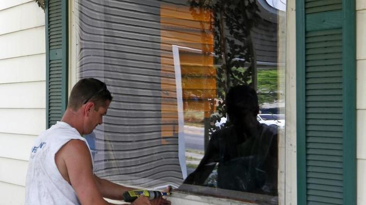 Repairman Joe Brougham uses a battery powered hand drill to screw in a custom-fit sheet of thick clear plastic over the front living room window of a home at 911 S. Alston Ave. in 2015.