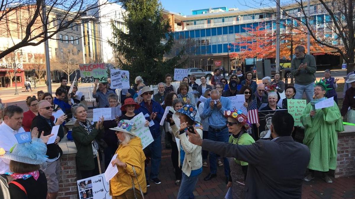 Faisal Khan, founder of the Carolina Peace Center, at podium with back to camera, speaks to demonstrators at the “Rally to Stop the Trump-GOP Tax Scam” at CCB Plaza in downtown Durham Sunday.