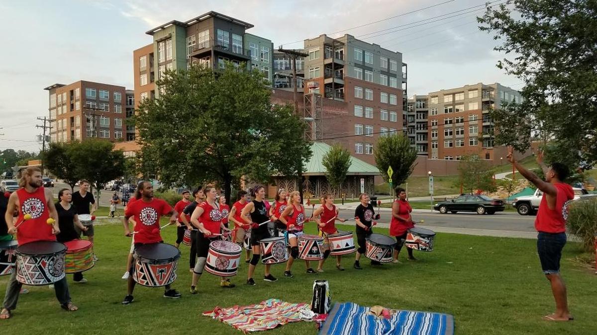 Batala Durham drumming group rehearses on Monday evenings during the summer at Durham Central Park, but at least one neighbor in the new Liberty Warehouse Apartments, pictured behind them, has called the police to complain. On Monday, Aug. 14, practice went off with no police response, and the drummers moved from the farmers’ market shelter to the open field as they finished.