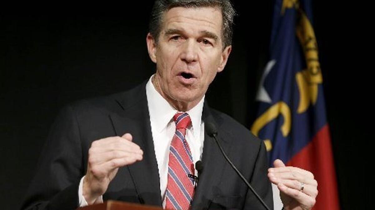 Gov. Roy Cooper speaks with a North Carolina flag over his shoulder.
