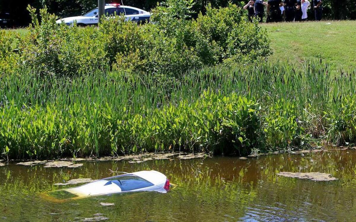 Pictured is the car that plunged into a pond off South Alston Avenue Wednesday. Police responded in time to rescue a pair of women, one of them pregnant, who were in the car when it began to sink. Durham police officers and bystanders look on from top of hill.