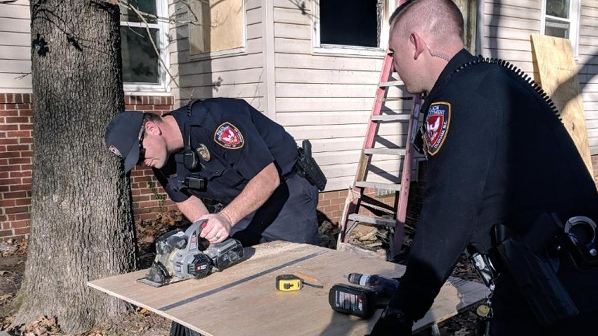 Durham Police Officers B.L. Taylor and D.R. Johnson cut plywood panels to cover the windows and door of a house that was damaged in a Nov. 18, 2017, fire.