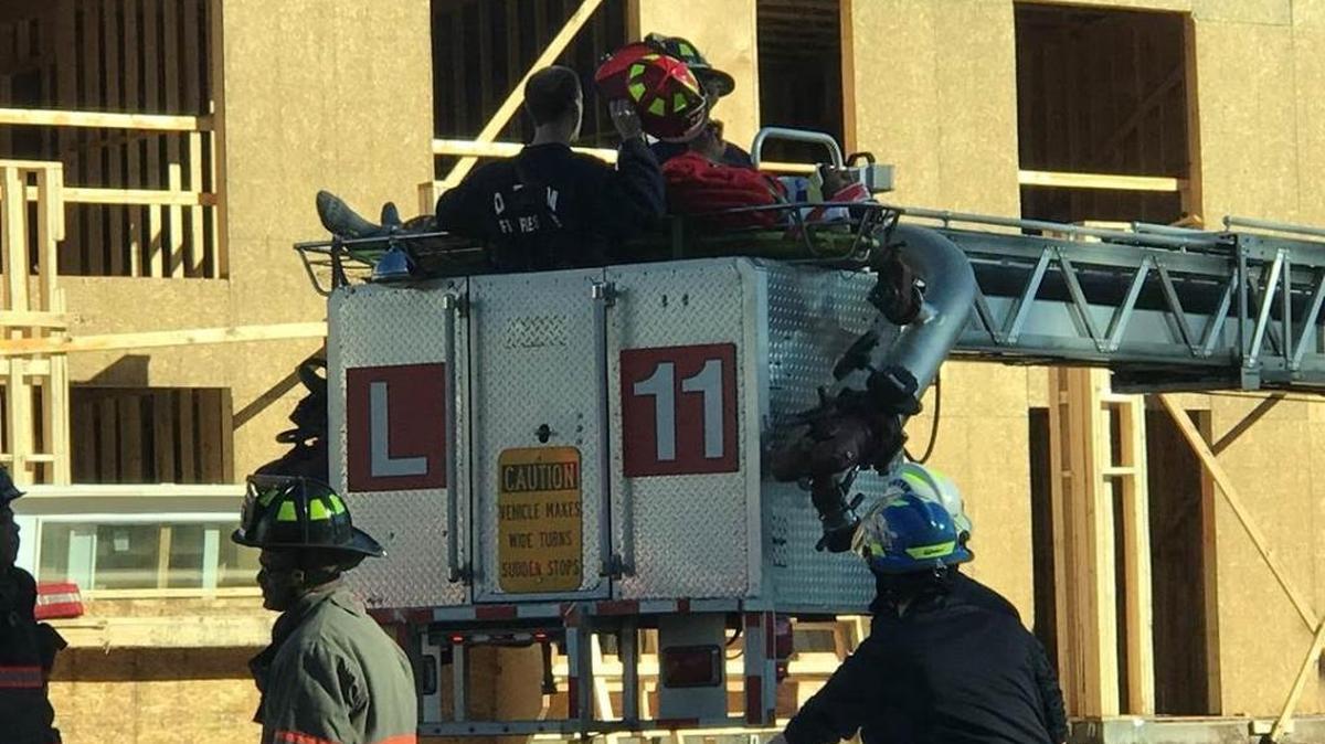 An injured construction worker is lowered to the ground in a fire truck’s ladder basket.