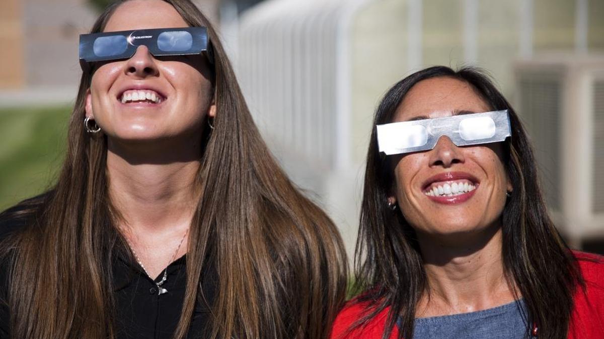 In this Tuesday, July 18, 2017 photo, Twin Falls High School science teachers Ashley Moretti, left, and Candace Wright, right, use their eclipse shades to look at the sun as they pose for a portrait at Twin Falls High School in Twin Falls, Idaho. The district bought 11,000 pairs of solar glasses, enough for every student and staff member to view the solar eclipse Aug. 21, from Twin Falls.