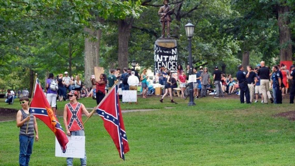 Two of the five men carrying Confederate flags stand near a sit-in at the base of the Silent Same Confederate statue (background) on the UNC campus Saturday, Aug. 26, 2017. The men carrying the flags were in opposition to the sit-in group who is calling for the removal of the Silent Sam. The men refused to give their names.