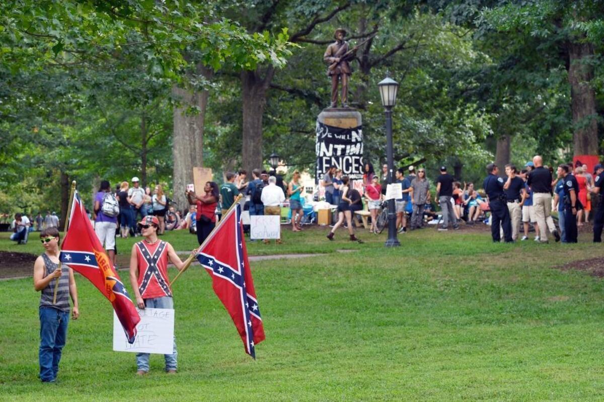Two of the five men carrying Confederate flags stand near a sit-in at the base of the Silent Same Confederate statue (background) on the UNC campus Saturday, Aug. 26, 2017. The men carrying the flags were in opposition to the sit-in group who is calling for the removal of the Silent Sam. The men refused to give their names.