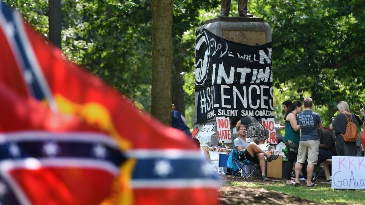 Confederate flags, foreground, flutter in the breeze about 50 yards from a group of protesters at the base of the Confederate statue know as Silent Sam on the UNC-Chapel Hill campus. Five men carrying Confederate flags showed up Saturday, Aug. 26, 2017, in opposition of the larger group calling for the statue’s removal.