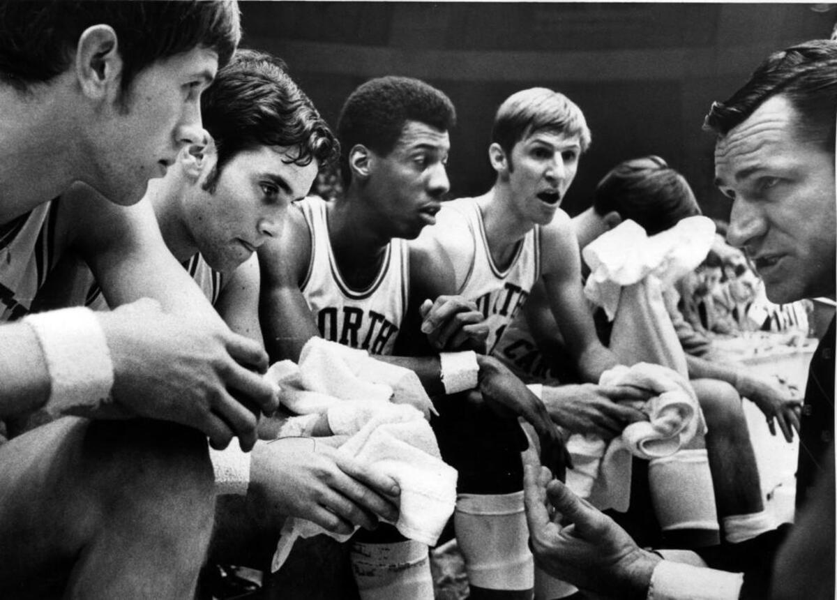 Dean Smith coached UNC teams to three straight Final Fours from 1967-69. The coach died in 2015. When Charlie Scott was inducted into the Naismith Basketball Hall of Fame in 2018, he honored Smith with a lapel button bearing Smith’s initials.