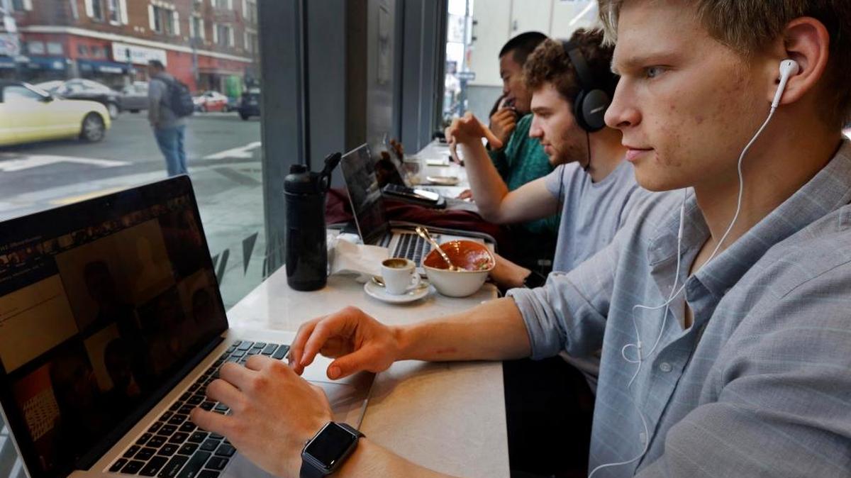 Connor Mitchell, right, works on a computer at a cafe in San Francisco. With college costs rising steadily and with more courses available online for free, some observers are beginning to question the need for a traditional college education that may include lectures on Greek philosophy but burden students with massive debt. Mitchell's university classes take place online through Minerva, he doesn't have any exams and he studies in a different country every year.