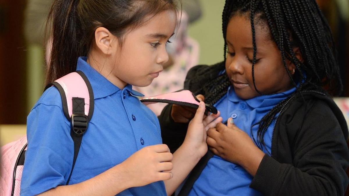 Mother Teresa Academy second graders Daymia Ramirez, 8, left, gets some help with her book bag from Emmora Thomas, 7, right, before leaving class in Erie, Pa.