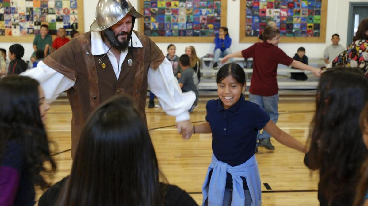 In this Wednesday, Aug. 30, 2017 photo, Edwin Quintana, left, dances with fifth grader Kaylee Pacheco and other students at Tesuque Elementary school in Tesuque, N.M. The students and others in Santa Fe's public school district were allowed to skip the annual presentation of Spanish colonial culture and history that honors a 17th century conquistador, in deference to Native American students and others who may find the performances disrespectful. None opted out in Tesuque. Public statues and tributes to early Spanish conquerors are enduring increased criticism tied to the brutal treatment of American Indians centuries ago by soldiers and missionaries.