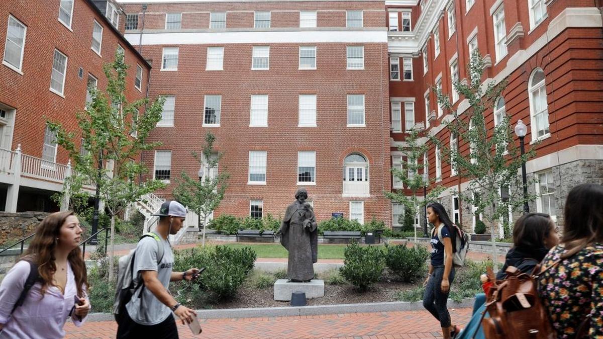 FILE - In this Sept. 1, 2016, file photo, students walk past a Jesuit statue in front of Freedom Hall, center, formerly named Mulledy Hall, on the Georgetown University campus, Thursday, Sept. 1, 2016, in Washington. Freedom Hall was renamed Isaac Hawkins Hall on April 19, 2017, in honor of the first person listed in documents related to an 1838 sale of slaves in order to pay off the school's debts. The school and the group of Catholic priests that founded it apologized for the sale.