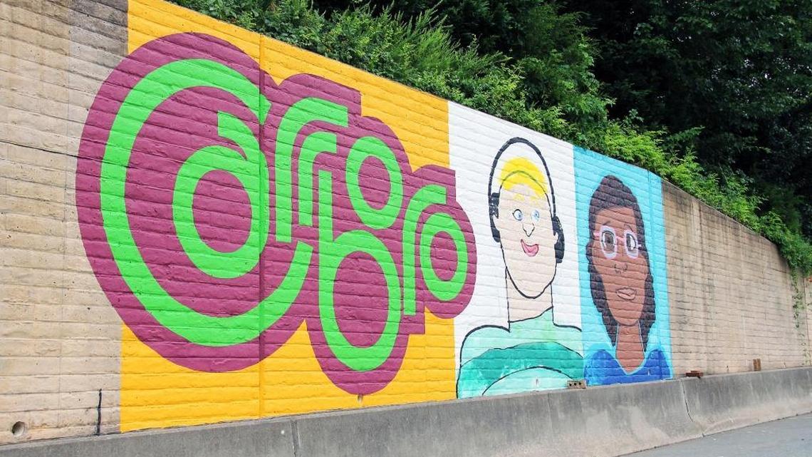 Chapel Hill artist Michael Brown’s mural, shown here mid-progress on the N.C. 54 off ramp to Jones Ferry Road in Carrboro, is painted in the style of children’s drawings and meant to celebrate the town’s diversity.
