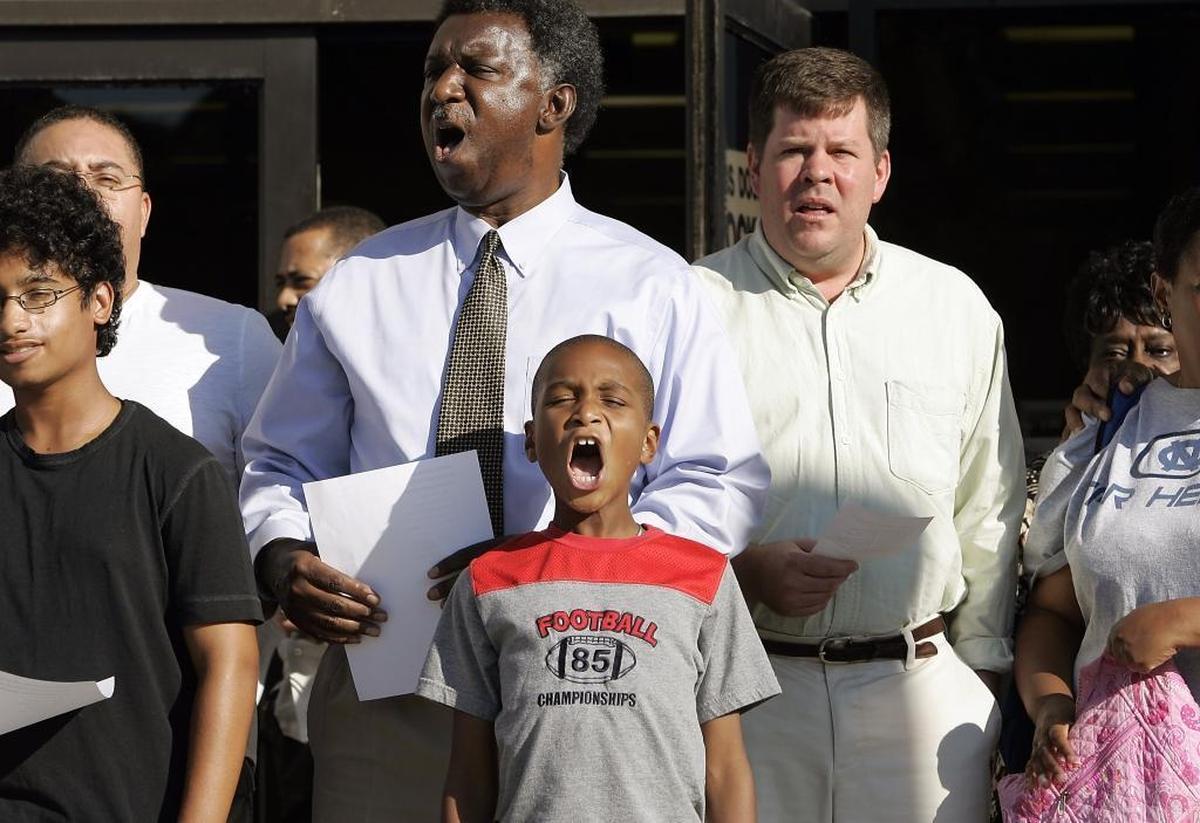 Durham City Council member Eddie Davis, whose term was from 2013 to 2017, is pictured here in 2007 when he was president of the NC Assocation of Educators. Davis, a retired Hillside High School teacher, is standing immediately behind Sterling Ward, 9, of Raleigh, as they sing “We Shall Overcome” following a discussion about the Royal Ice Cream sit-in here in 1957. Also pictured is community leader John Schelp, right.