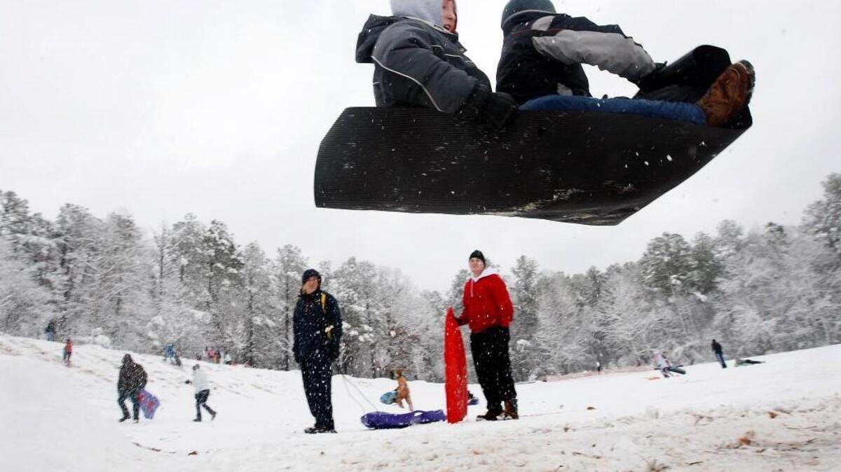 Sledders go airborne after piloting their mat over a ramp made of packed snow at Bond Park in Cary in December 2010.