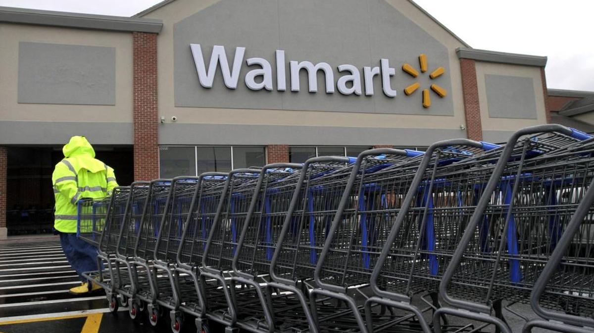 A worker pulls a line of shopping carts toward a Wal-Mart store. Starting in February, the starting wages of Wal-Mart associates will increase to $11 an hour.