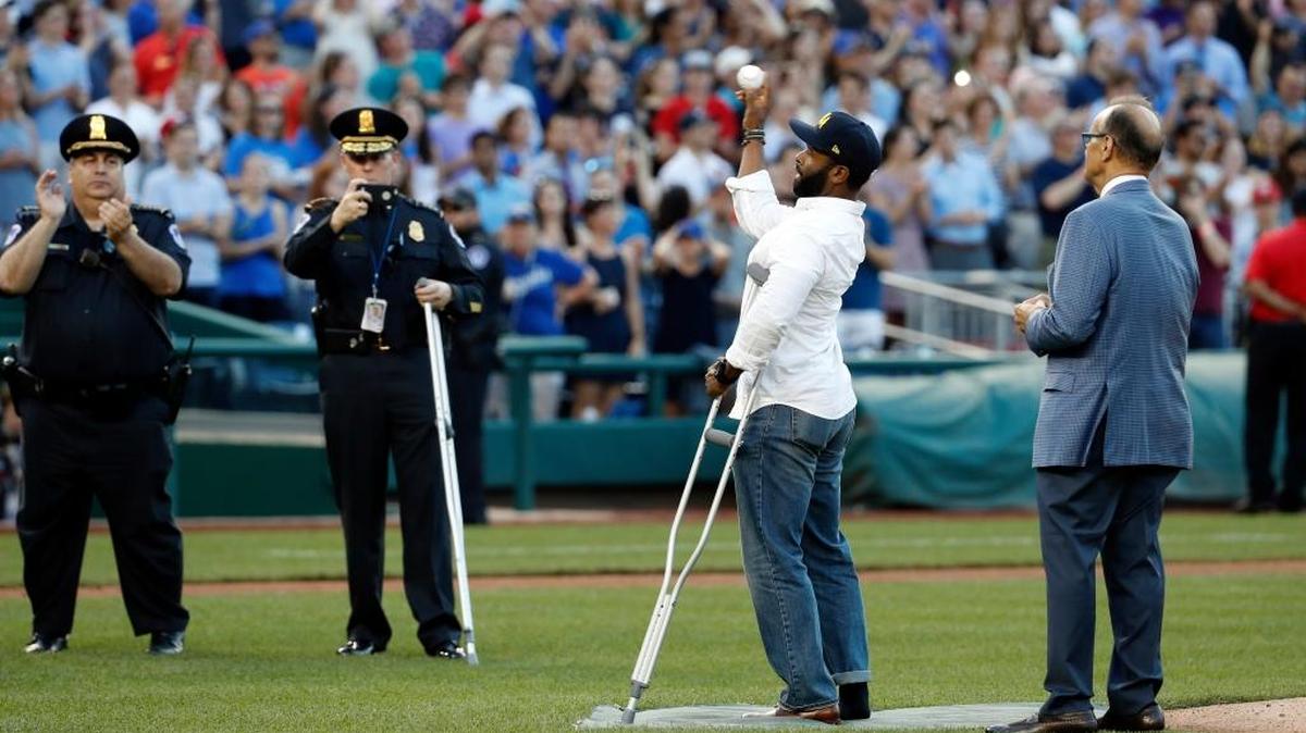 Injured Capitol Hill Police officer David Bailey throws out a ceremonial first pitch with Joe Torre, MLB's Chief Baseball Officer, right, watching, before the Congressional baseball game, Thursday, June 15, 2017, in Washington.