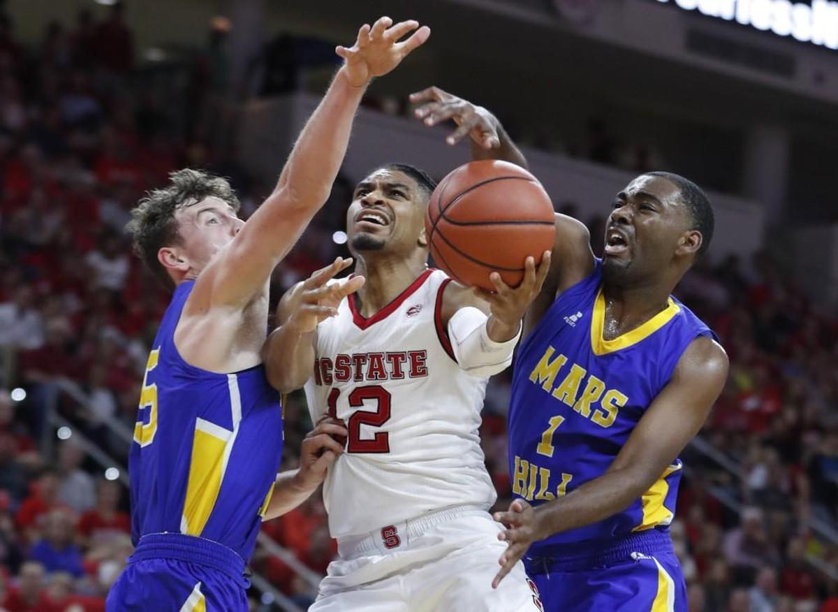 N.C. State's Allerik Freeman (12) drives between Mars Hill’s Brandon Watkins (35), left, and Nassyr Daniel (1) during the exhibition game at PNC Arena Friday, Nov. 3, 2017.