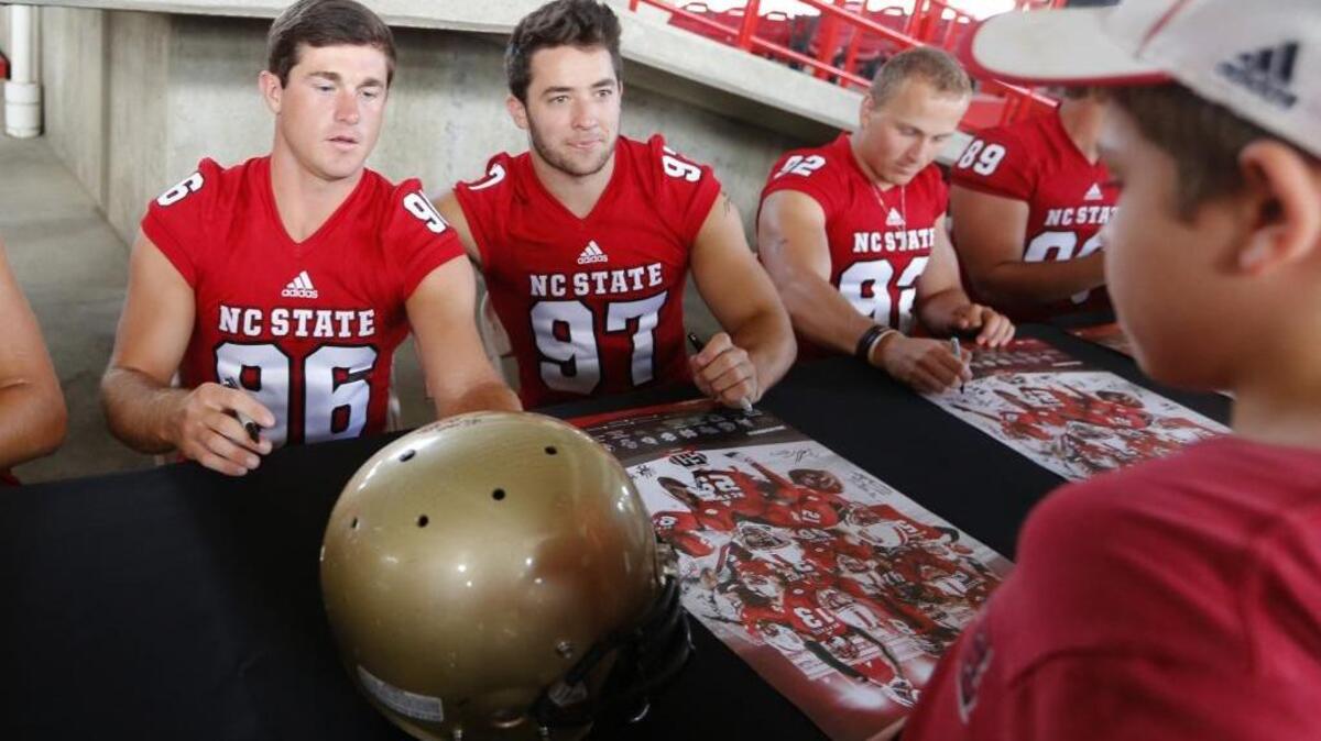 N.C. State’s Connor Haskins, left, signs a helmet for a fan during the Wolfpack’s Meet the Pack day on Sunday. To Haskins’ right are Jackson Maples and Kyle Bambard.